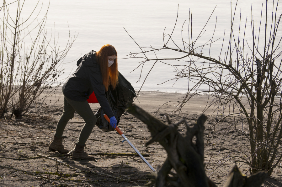 Volunteer Raechal Burke reaches to pick up a piece of trash on Saturday at Marine Park. Vancouver&#039;s Water Resources Education Center hosted eight masked volunteers in a spring cleanup of the park and its beach.