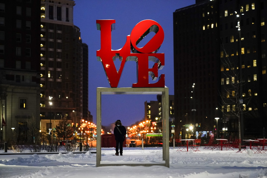 A person wearing a face mask as a precaution against the coronavirus walks during a winter storm near the Robert Indiana sculpture &quot;LOVE&quot; at John F. Kennedy Plaza, commonly known as Love Park, in Philadelphia, Monday, Feb. 1, 2021.