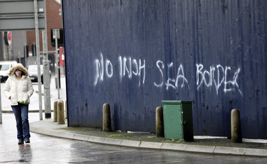 A woman walks past past graffiti with the words &#039;No Irish Sea Border&#039; in Belfast city centre, Northern Ireland, Wednesday, Feb. 3, 2021. Politicians from Britain, Northern Ireland and the European Union are meeting to defuse post-Brexit trade tensions that have shaken Northern Ireland&#039;s delicate political balance. British Cabinet minister Michael Gove, European Commission Vice President Maros Sefcovic and the leaders of Northern Ireland&#039;s Catholic-Protestant power-sharing government will hold a video conference to discuss problems that have erupted barely a month after the U.K. made an economic split from the 27-nation EU.