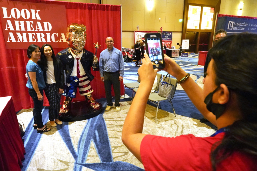 Conference attendees pose for a photo next to a statue of former president Donald Trump at the merchandise show at the Conservative Political Action Conference (CPAC) Saturday, Feb. 27, 2021, in Orlando, Fla.