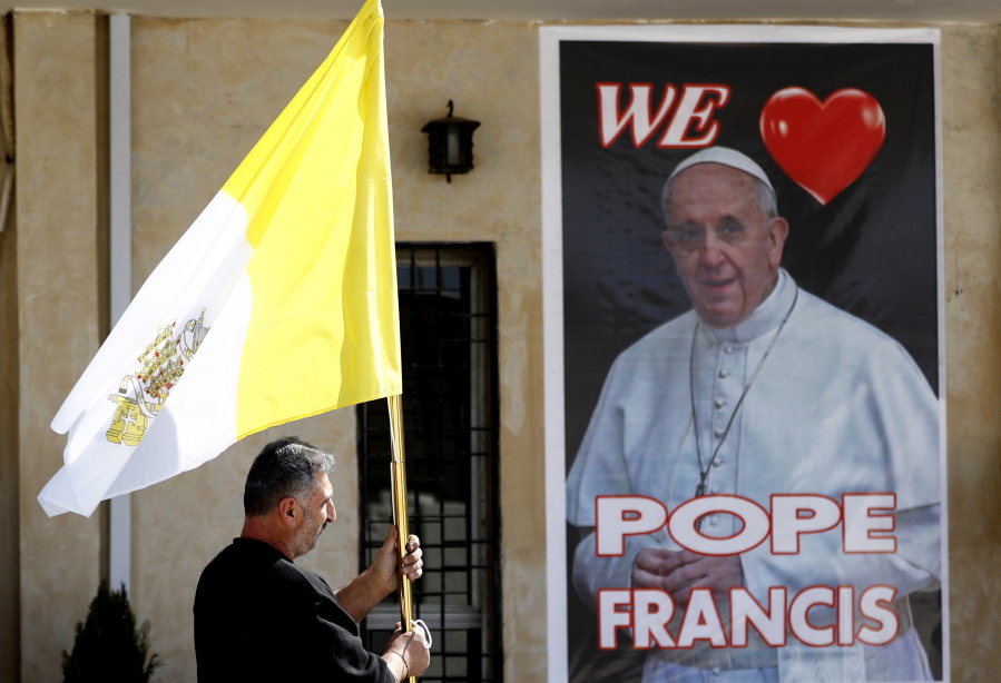 A Christian priest holds a Vatican flag as he walks by a poster of Pope Francis during preparations for the Pope&#039;s visit in Mar Youssif Church in Baghdad, Iraq, Friday, Feb. 26, 2021.