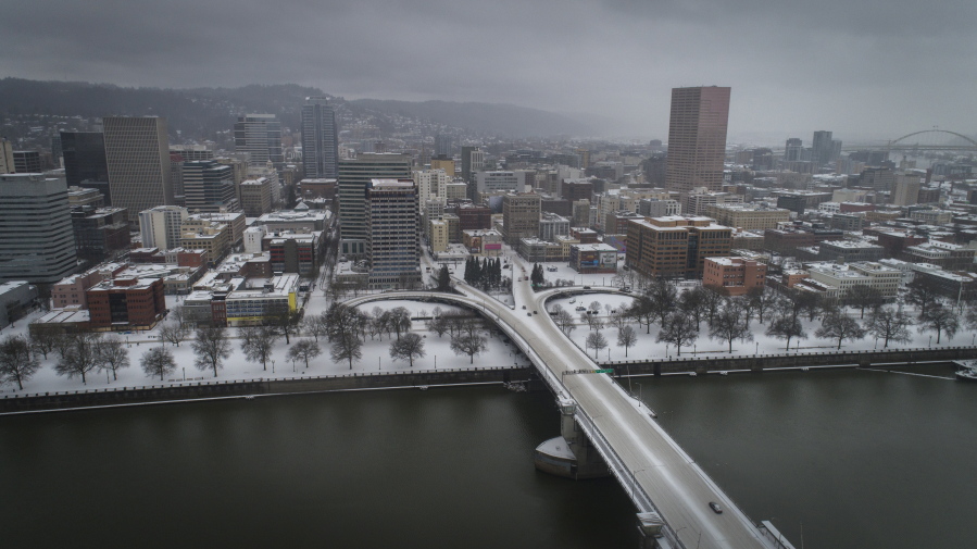 An aerial view of the Morrison Bridge and downtown Portland, Ore., is seen during a snowstorm, on Friday, Feb. 12, 2021. A winter storm has blanketed the Pacific Northwest with ice and snow, leaving hundreds of thousands of people without power and disrupting travel across the region.