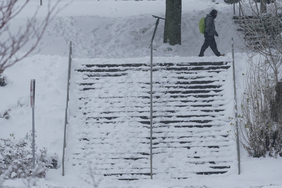 A pedestrian walks near a snow-covered staircase, Saturday, Feb. 13, 2021, on the University of Washington campus in Seattle. Winter weather was expected to continue through the weekend in the region.(AP Photo/Ted S.