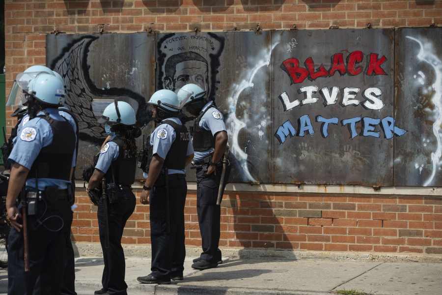 FILE - In this Aug. 15, 2020, file photo, police officers stand beside a mural for George Floyd in the Chicago neighborhood of Bronzeville during an anti-police brutality protest. In the last decade, high-profile police killings  -- including Floyd -- have shaken the nation and led to widespread protests and calls for reform, including hiring more nonwhite and female officers.