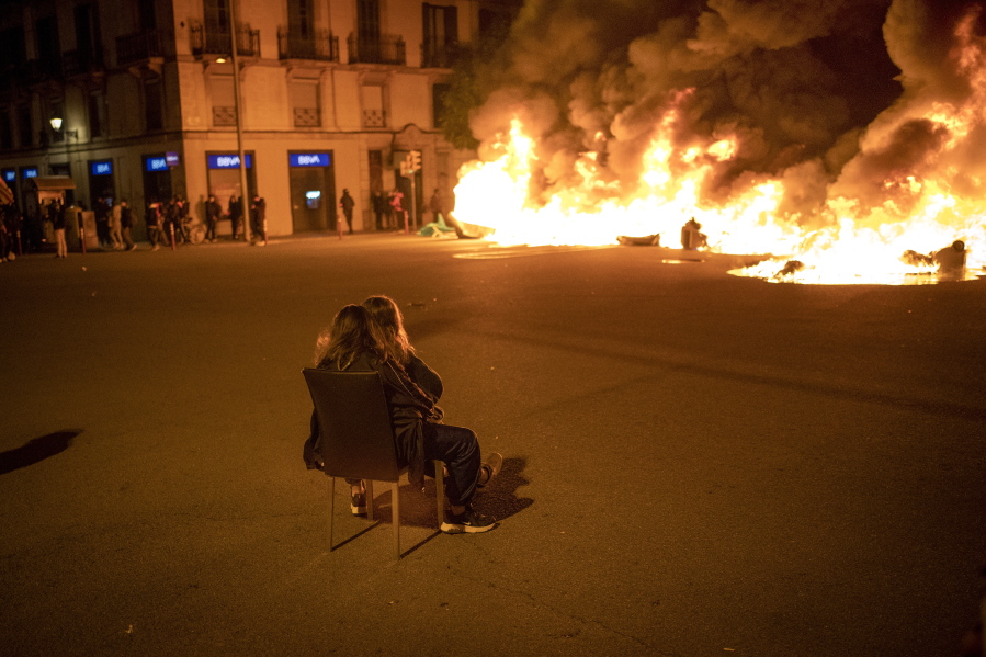 Two women sit on a chair in front of burning barricades made by demonstrators during a protest condemning the arrest of rap singer Pablo Hasel in Barcelona, Spain, Friday.