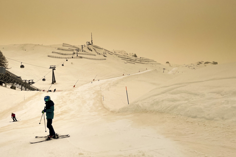 Skiers wearing protective face mask ski as Sahara sand colours the snow and the sky in orange and creates a special light atmosphere, during the coronavirus disease (COVID-19) outbreak, in the Alpine resort of Anzere, Switzerland, on Saturday, 6 February 2021.