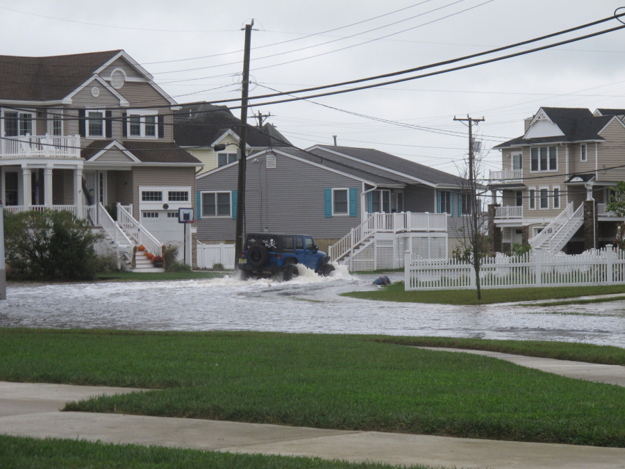 A vehicle kicks up a wake as it drives through a flooded street in Ocean City, N.J. on Oct. 30, 2020. The city is dealing with the costs of rising sea levels, both in monetary terms and in the disruption that recurring flooding brings.