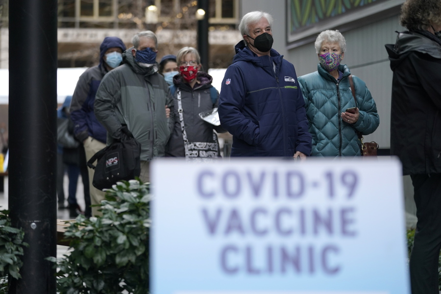 FILE - In this an. 24, 2021, file photo, people stand near a sign as they wait in line to receive the first of two doses of the Pfizer vaccine for COVID-19 at a one-day vaccination clinic set up in an Amazon.com facility in Seattle and operated by Virginia Mason Franciscan Health. Scientists say it&#039;s still too early to predict the future of the coronavirus, but many doubt it will ever go away entirely. (AP Photo/Ted S.