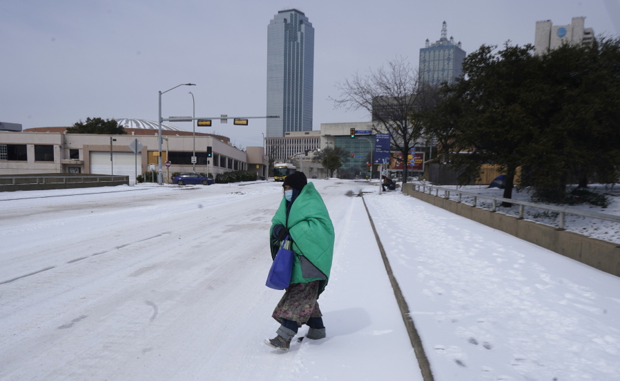 FILE - In this Feb. 16, 2021, file photo, a woman wrapped in a blanket crosses the street near downtown Dallas. As temperatures plunged and snow and ice whipped the state, much of Texas&#039; power grid collapsed, followed by its water systems. Tens of millions huddled in frigid homes that slowly grew colder or fled for safety.