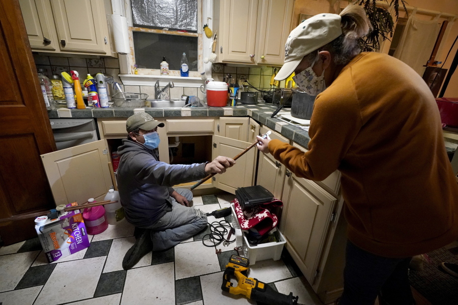 FILE - In this Feb. 20, 2021, file photo, Handyman Roberto Valerio, left, hands homeowner Nora Espinoza the broken pipe after removing it from beneath her kitchen sink in Dallas. The pipe broke during freezing temperatures brought by last week&#039;s winter weather.