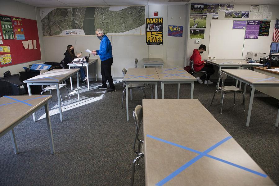 Desks at Heritage High School are marked for social distancing as sophomore Mya Beasley, 15, receives a math worksheet from geometry teacher Dwight Patterson on Thursday morning while joined by fellow sophomore Jayden Garcia, 15. Teachers and staff in Evergreen Public Schools welcomed back students in all high school grades for the first time since March 13, 2020, when schools closed due to COVID-19 concerns.