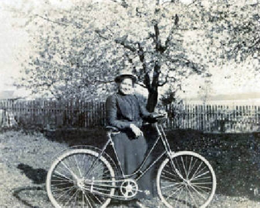Matilda Stanger Overand shows off her bicycle. While machinists had adapted bicycles for women, clothing designers were farther behind. Although this model has a rear bumper to protect its rider from backsplashes, it lacks a chain guard and is a bit tall for its rider. This helps date the photo to the 1890s. Her father, John Stanger, was a Scotsman who arrived in the area with the Hudson&#039;s Bay Company in 1838.