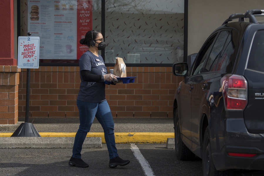 Service team member Selena, who declined to give her last name, serves a customer using the new curbside pickup app at Burgerville Heritage Plaza on Monday afternoon. The company added a tracking option last week through an app called FlyBuy that allows the restaurant to know exactly when customers pull in.