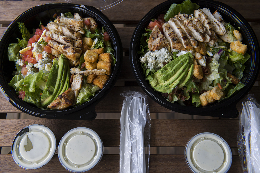 Avo-Cobb-O salads from Red Robin Gourmet Burgers and Brews, left, and Fresh Set are pictured in their delivery packaging. Fresh Set is one of three &quot;virtual brands&quot; from Red Robin that operates exclusively on delivery apps like DoorDash. At top, the salads are shown listed at Red Robin, left, and Fresh Set on the DoorDash app.