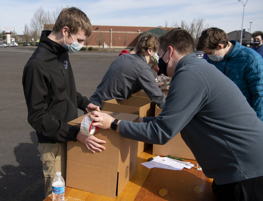 Boy Scout Troop 358 member Grant Myers, left, assists as Daniel Forster, 17, tapes a box of food on Saturday in the Living Hope Church parking lot. The Fort Vancouver Lions Club organized the one-off food drive event Saturday, modeled after December&#039;s Drive &amp; Drop event.