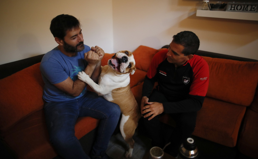 Former Catholic priest Andres Gioeni, right, sits Wednesday with his husband, Luis Iarocci, and their dog Boris after they got home from the bishopric where he started the process of apostasy in Buenos Aires, Argentina.