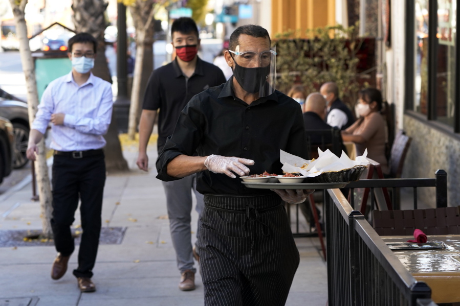 FILE - A waiter wears a mask and face covering at a restaurant with outdoor seating Tuesday, Dec. 1, 2020, in Pasadena, Calif.  The U.S. services sector, where most Americans work, registered its sixth consecutive month of expansion in November. The Institute for Supply Management reported Thursday that its index of services activity declined slightly to a reading of 55.9 last month, from a reading of 56.6 in October.
