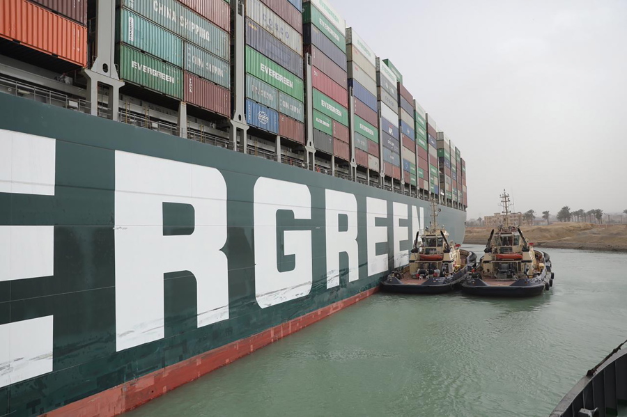 This photo released by the Suez Canal Authority on Thursday, March 25, 2021, shows two tugboats next to the Ever Given, a Panama-flagged cargo ship, after it become wedged across the Suez Canal and blocking traffic in the vital waterway from another vessel. An operation is underway to try to work free the ship, which further imperiled global shipping Thursday as at least 150 other vessels needing to pass through the crucial waterway idled waiting for the obstruction to clear.