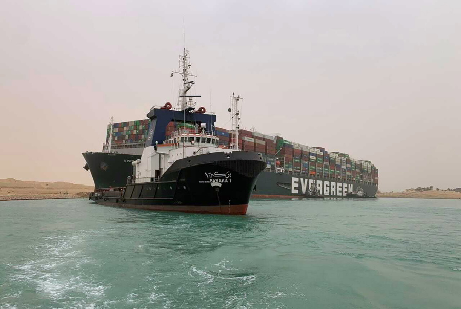 In this photo released by the Suez Canal Authority, a boat navigates in front of a massive cargo ship, named the Ever Green, rear, sits grounded Wednesday, March 24, 2021, after it turned sideways in Egypt&#039;s Suez Canal, blocking traffic in a crucial East-West waterway for global shipping. An Egyptian official warned Wednesday it could take at least two days to clear the ship.