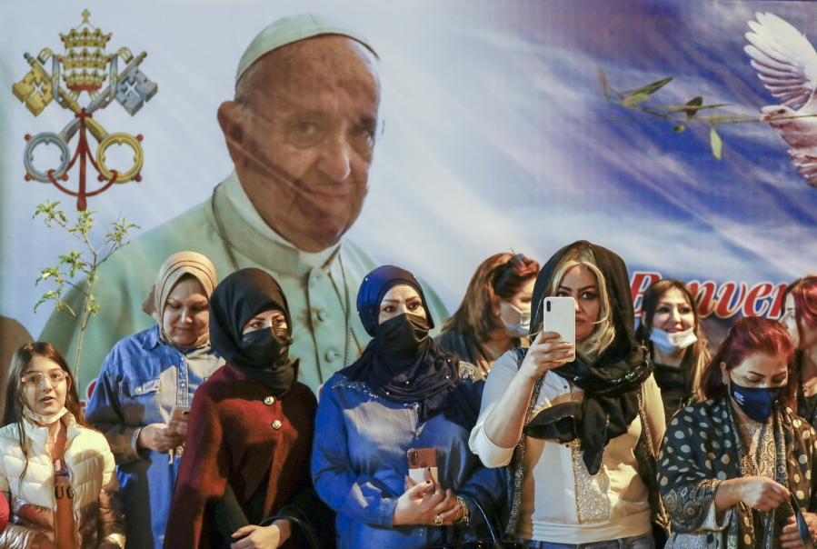 Women wait outside the Chaldean Cathedral of Saint Joseph, in Baghdad, Iraq, Saturday, March 6, 2021, where Pope Francis, depicted on a giant poster at their back, is concelebrating a mass. Earlier today Francis met privately with the country&#039;s revered Shiite leader, Grand Ayatollah Ali al-Sistani.
