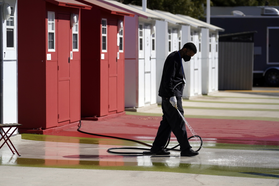 A worker cleans in front of a row of tiny homes for the homeless, Thursday, Feb. 25, 2021, in the North Hollywood section of Los Angeles.