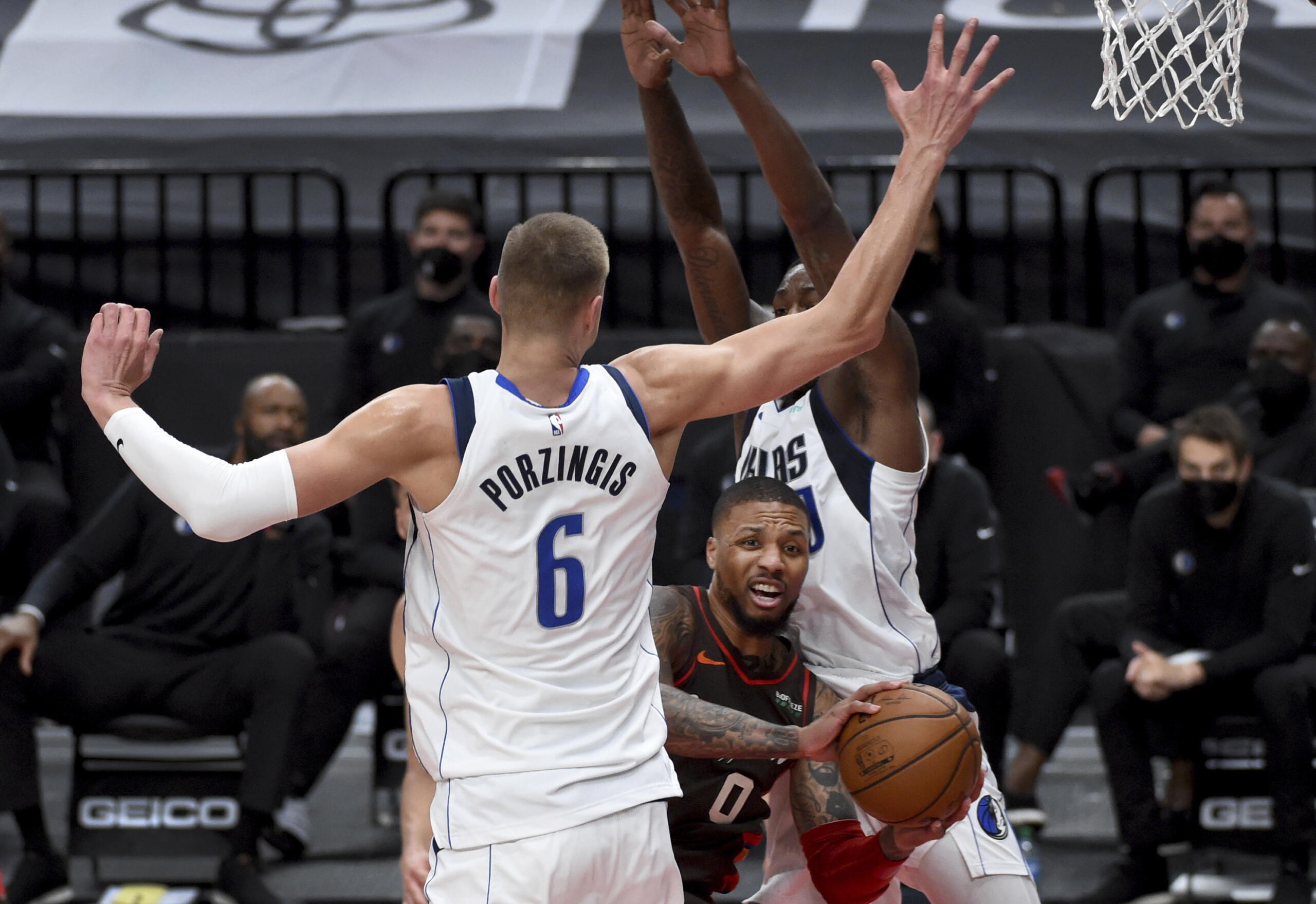 Portland Trail Blazers guard Damian Lillard, middle, passes the ball on Dallas Mavericks center Kristaps Porzingis, left, during the second half of an NBA basketball game in Portland, Ore., Sunday, March 21, 2021.