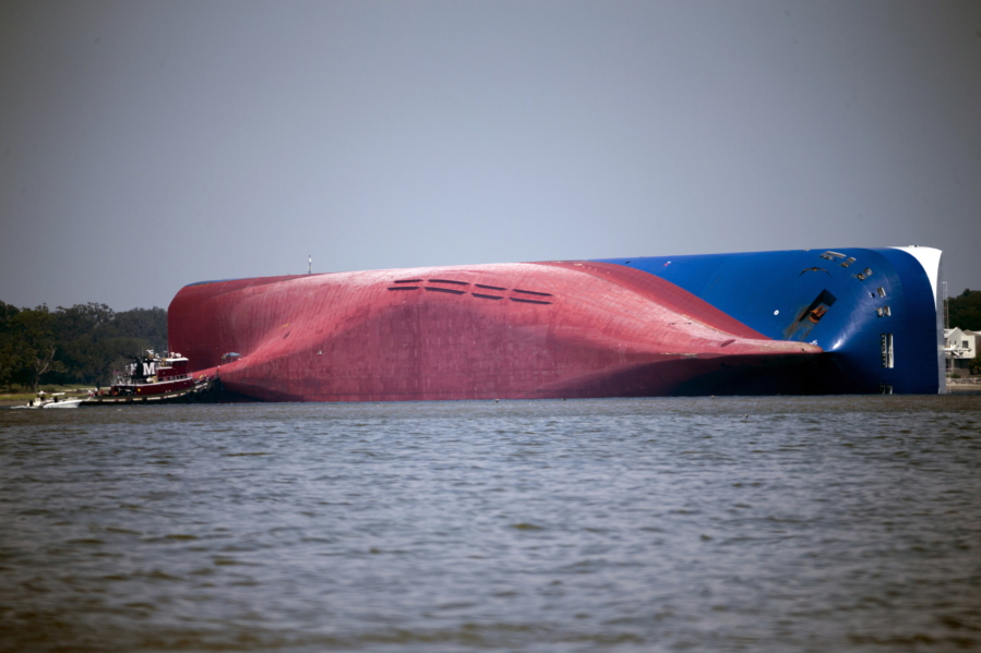 FILE - In this Sept. 9, 2019, file photo, a Moran tugboat nears the stern of the capsizing vessel Golden Ray near St. Simons Sound off the coast of Georgia. Demolition of the large cargo ship along the coast of Georgia is entering its fifth month, with work to chop the ship into eight large pieces going far slower than the salvage crew anticipated. (AP Photo/Stephen B.