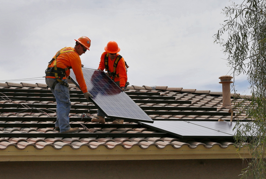 FILE - In this July 28, 2015, file photo, electricians, Adam Hall, right, and Steven Gabert install solar panels on a roof for Arizona Public Service company in Goodyear, Ariz. As states across the U.S. West beef up their renewable energy mandates, a push to do so in Arizona has been met by fierce resistance from the Republican governor and GOP-dominated Legislature.