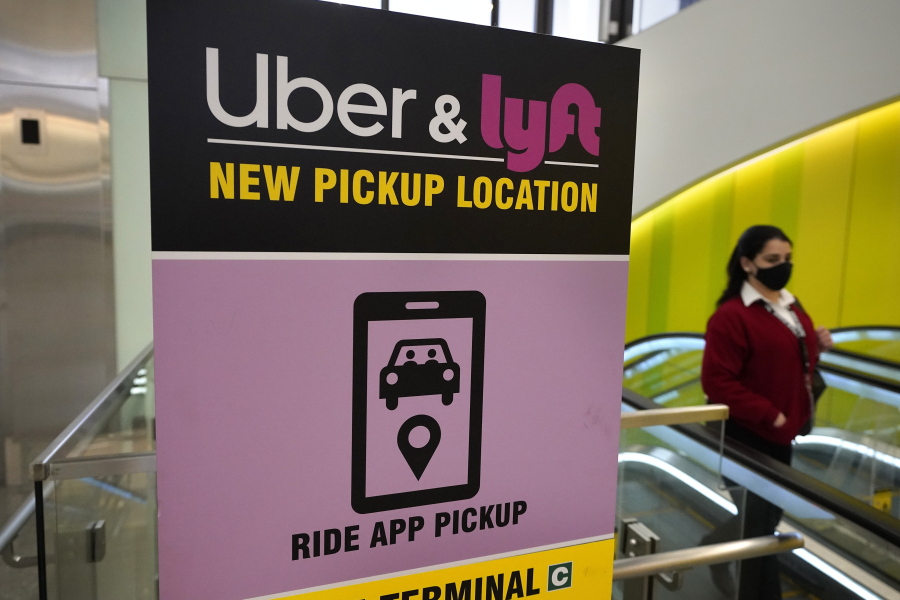 FILE - In this Feb. 9, 2021 file photo, a passer-by walks past a sign offering directions to an Uber and Lyft ride pickup location at Logan International Airport, in Boston.  Uber and Lyft have teamed up to create a database of drivers ousted from their ride-hailing services for complaints about sexual assault and other crimes that have raised passenger-safety concerns for years. The clearinghouse unveiled Thursday, March 11,  will initially list drivers expelled by the ride-hailing rivals in the U.S.