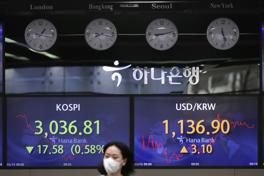 A currency trader walks near screens showing the Korea Composite Stock Price Index (KOSPI), left, and the foreign exchange rate between U.S. dollar and South Korean won at the foreign exchange dealing room in Seoul, South Korea, Monday, March 15, 2021. Shares were mixed in Asia on Monday as China reported a variety of data that painted a complicated picture of its recovery from the pandemic.