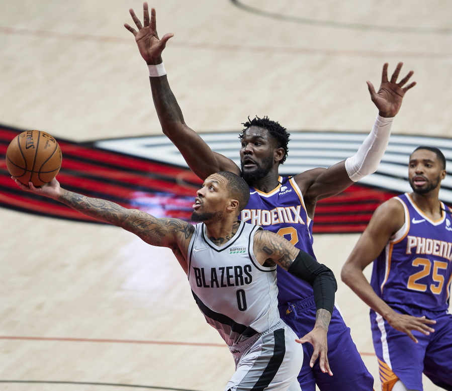 Portland Trail Blazers guard Damian Lillard, left, shoots next to Phoenix Suns center Deandre Ayton during the second half of an NBA basketball game in Portland, Ore., Thursday, March 11, 2021.