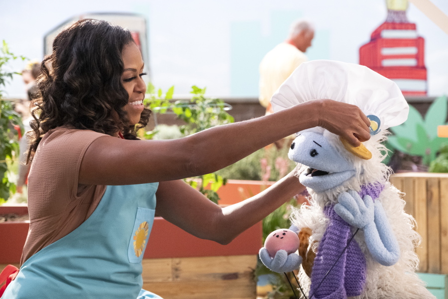 This image released by Netflix shows former first lady Michelle Obama putting a chef&#039;s hat on Waffles, a furry puppet with waffle ears and holding Mochi, a pink round puppet, on the set of the children&#039;s series &quot;Waffles + Mochi.&quot; Obama is launching the new Netflix children&#039;s food show on March 16.