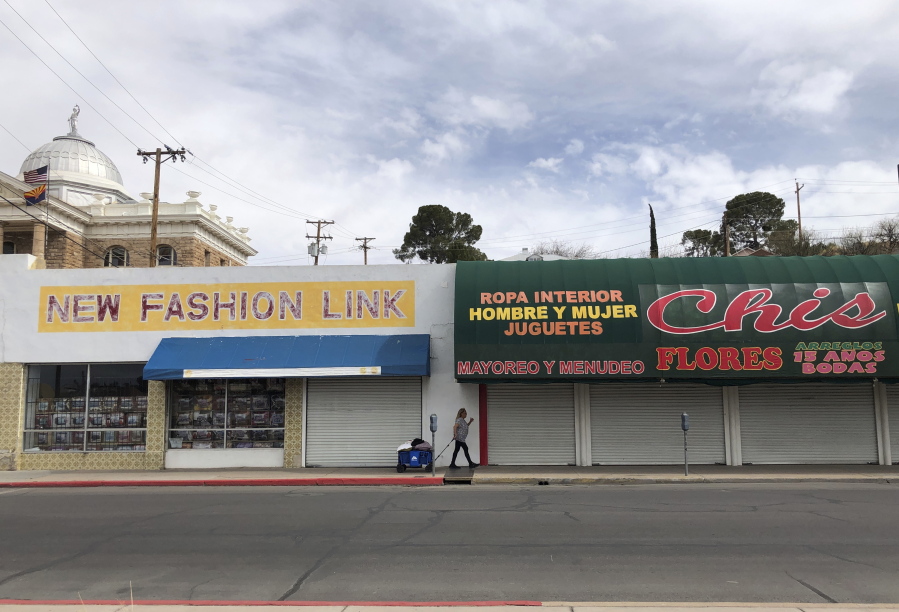 A woman walks past two out-of-business clothing stores located steps away from the U.S.-Mexico border on March 15, 2021 in Nogales, Ariz. The economic wear from nearly 12 months of a partially shut border is easy to spot in downtown Nogales. Bargain clothing stores, money exchanges, secondhand shops and retailers selling plastic knickknacks within walking distance of the border stand closed and many storefronts are boarded up.