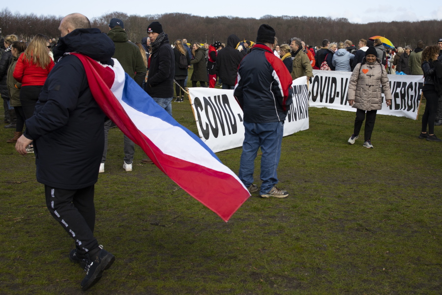 A man wearing a Dutch flag passes signs reading &quot;COVID Rules = Dictatorship&quot; and &quot;COVID Vaccin = Poison&quot; during a demonstration ahead of three days of voting starting Monday in a general election, to protest government policies including the curfew, lockdown and coronavirus related restrictions in The Hague, Netherlands, Sunday, March 14, 2021.