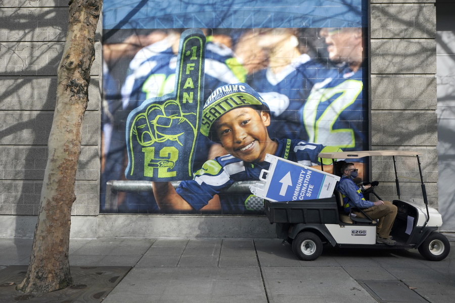 A cart carries a sign that reads &quot;Community Vaccination Site,&quot; past a photo of a Seattle Seahawks fan, Saturday, March 13, 2021, on the first day of operation of a mass COVID-19 vaccination site at the Lumen Field Events Center in Seattle, which adjoins the field where the NFL football Seahawks and the MLS soccer Seattle Sounders play their games. The site, which is the largest civilian-run vaccination site in the country, will operate only a few days a week until city and county officials can get more doses of the vaccine. (AP Photo/Ted S.