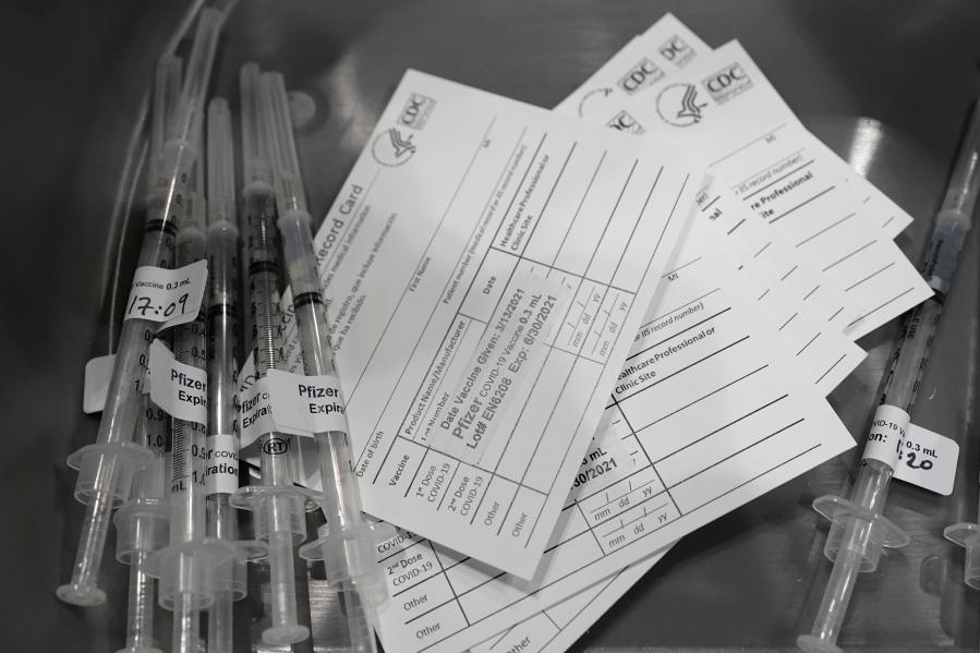 Syringes with doses of the Pfizer COVID-19 vaccine, are shown next to vaccination cards, Saturday, March 13, 2021, on the first day of operations at a mass vaccination site at the Lumen Field Events Center in Seattle, which adjoins the field where the NFL football Seattle Seahawks and the MLS soccer Seattle Sounders play their games. The site, which is the largest civilian-run vaccination site in the country, will operate only a few days a week until city and county officials can get more doses of the vaccine. (AP Photo/Ted S.