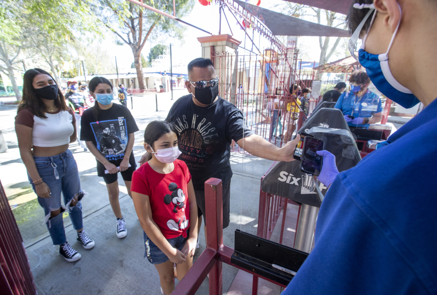 Customer Cesar Romero, with niece Valeria Ocampo, holds his phone showing a bar code so that it can be scanned by employee Daniel Abidin, right, at the entrance to Six Flags Magic Mountain in Valencia, California, which re-opened on April 2, 2021, after more than a year of being closed due to the coronavirus outbreak.