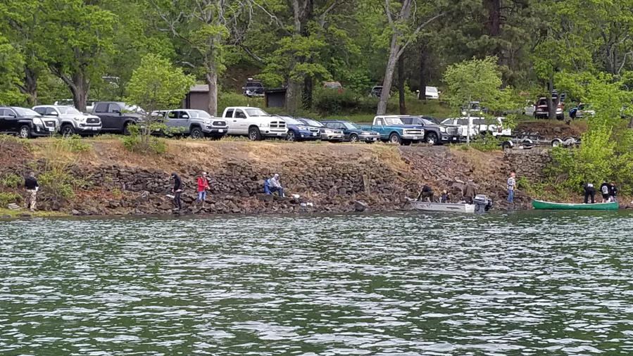 Anglers fish from the bank and launch small boats at Rowland Lake on Saturday, April 24, 2021. The crowded parking lot behind them is a testament to the popularity of the spring trout opener.
