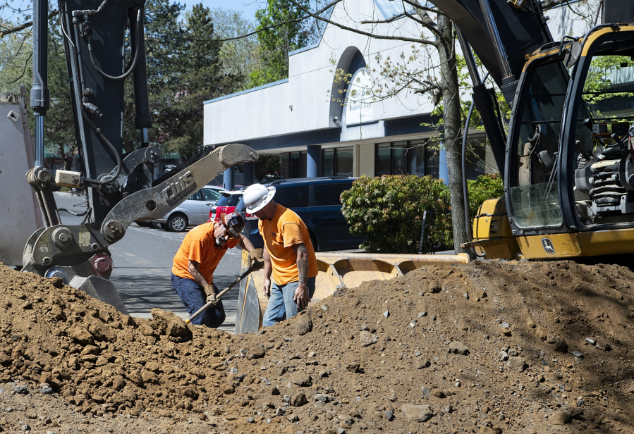 A pair of construction workers shovel large chunks of pavement into the excavator on Tuesday at the corner of Broadway and East Mill Plain Boulevard. The work marks the start of a project to replace the sewer and water main lines beneath Broadway, which will continue through the summer.
