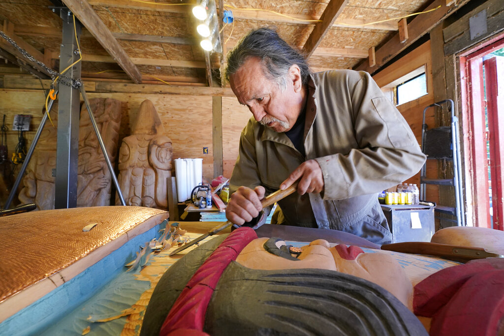 Lummi Nation lead carver Jewell James works on the final details of a nearly 25-foot totem pole to be gifted to the Biden administration, Monday, April 12, 2021, on the Lummi Reservation, near Bellingham, Wash. The pole, carved from a 400-year old red cedar, will make a journey from the reservation past sacred indigenous sites, before arriving in Washington, D.C. in early June. Organizers said that the totem pole is a reminder to leaders to honor the rights of Indigenous people and their sacred sites.