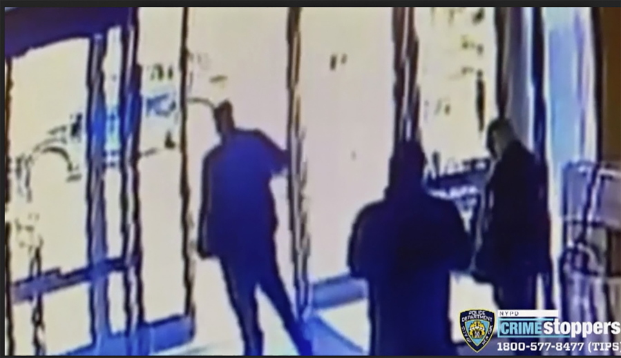 This image taken from surveillance video provided by the New York City Police Department shows an apartment building employee, center, closing the building&#039;s front door after a man assaulted a 65-year-old Asian American woman, Monday afternoon, March 29, 2021, a few blocks from New York&#039;s Times Square.