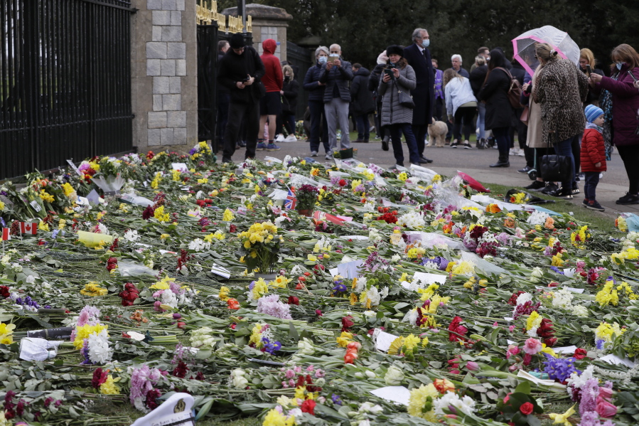 People look at flowers outside Windsor Castle in Windsor, England Sunday, April 11, 2021. Britain&#039;s Prince Philip, the irascible and tough-minded husband of Queen Elizabeth II who spent more than seven decades supporting his wife in a role that mostly defined his life, died on Friday.