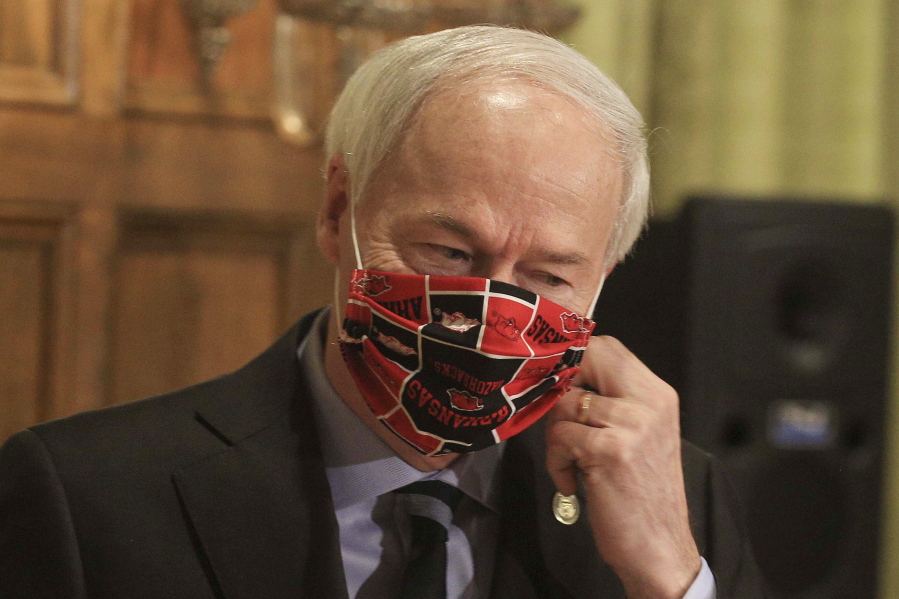 FILE - In this April 27, 2020, file photo, Gov. Asa Hutchinson takes off his Arkansas Razorbacks facemark as he arrives for the daily coronavirus briefing at the state Capitol in Little Rock. A longtime abortion opponent who once opposed allowing gay couples to be foster parents, Gov. Hutchinson is the unlikeliest figure to complain about bills on the &quot;culture wars&quot; reaching his desk.