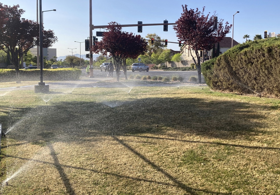 Sprinklers water grass near a street corner Friday, April 9, 2021, in the Summerlin neighborhood of northwest Las Vegas. A desert city built on a reputation for excess wants to become a model for restraint with a first-in-the-nation policy limiting water use by banning grass that nobody walks on.