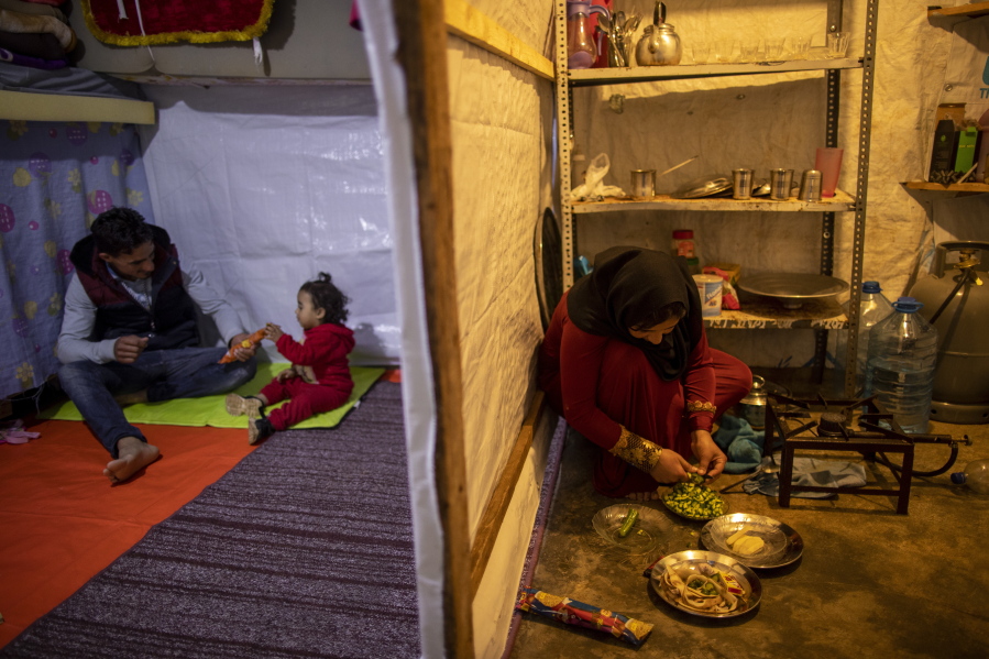 Syrian refugee Ayesha al-Abed, 21, right, prepares food as her Husband Raed Mattar, 24, left, plays with their daughter Rayan, 18 months old, before they break their fast on the first day of fasting month of Ramadan, at an informal refugee camp, in the town of Bhannine in the northern city of Tripoli, Lebanon, Tuesday, April 13, 2021. For many Syrian refugee families in Lebanon, Ramadan comes as a hard life of displacement has gotten even harder after a pandemic year that deepened economic woes in their host country.