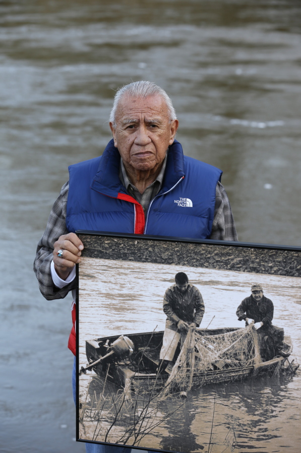 FILE - In this Monday, Jan. 13, 2014, file photo Billy Frank Jr., a Nisqually tribal elder who was arrested dozens of times while trying to assert his native fishing rights during the Fish Wars of the 1960s and '70s, poses for a photo while holding a late 1960s photo of himself, left, fishing with Don McCloud, near Frank's Landing on the Nisqually River in Nisqually, Wash. Gov. Jay Inslee on Wednesday, April 14, 2021, signed a measure that starts the process of honoring the late Frank, who championed treaty rights and protecting the environment with a statue at the U.S. Capitol. (AP Photo/Ted S.