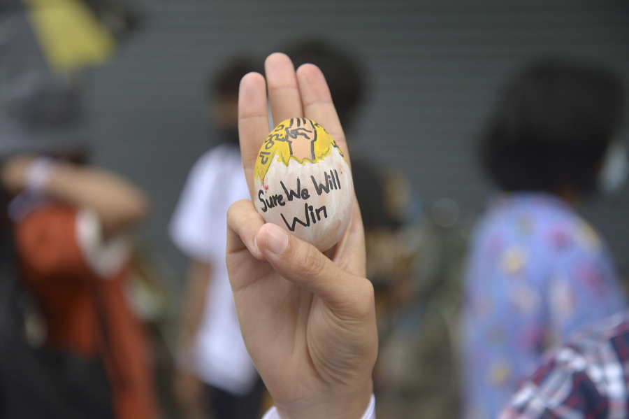 An anti-coup protester raises a decorated Easter egg along with the three-fingered symbol of resistance during a protest against the military coup on Easter Sunday, April 4, 2021, in Yangon, Myanmar.