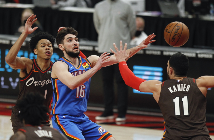 Oklahoma City Thunder guard Ty Jerome, center, passes as Portland Trail Blazers guard Anfernee Simons, left, and center Enes Kanter, right, defend during the first half of an NBA basketball game in Portland, Ore., Saturday, April 3, 2021.