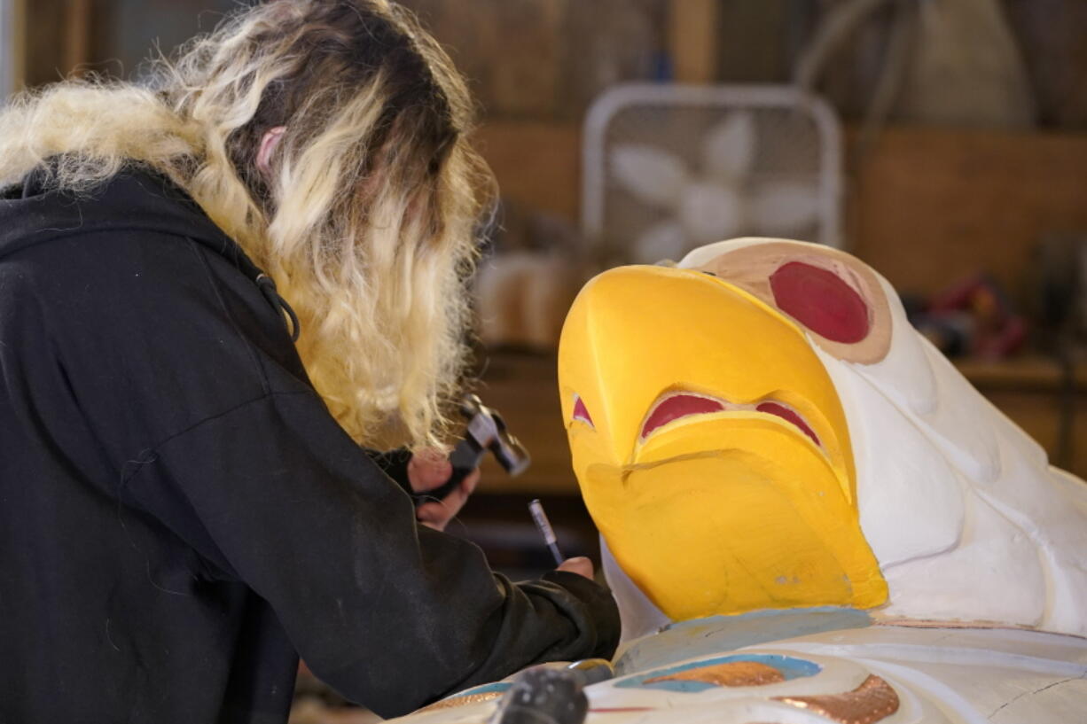 Lummi Nation member Jewell Ridley-James, son of lead carver Jewell James, helps to work on the final details of a diving eagle on a nearly 25-foot totem pole to be gifted to the Biden administration, Monday, April 12, 2021, on the Lummi Reservation, near Bellingham, Wash. The pole, carved from a 400-year old red cedar, will make a journey from the reservation past sacred indigenous sites, before arriving in Washington, D.C. in early June. Organizers said that the totem pole is a reminder to leaders to honor the rights of Indigenous people and their sacred sites.