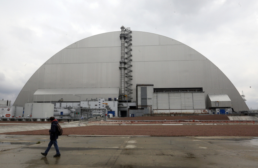 A man walks past a shelter covering the exploded reactor at the Chernobyl nuclear plant, in Chernobyl, Ukraine, Thursday, April 15, 2021. The vast and empty Chernobyl Exclusion Zone around the site of the world's worst nuclear accident is a baleful monument to human mistakes. Yet 35 years after a power plant reactor exploded, Ukrainians also look to it for inspiration, solace and income.